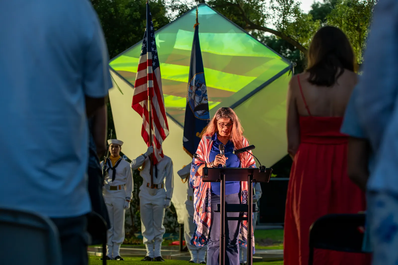 A vertical view frames the lectern speaker between audience members and flags.