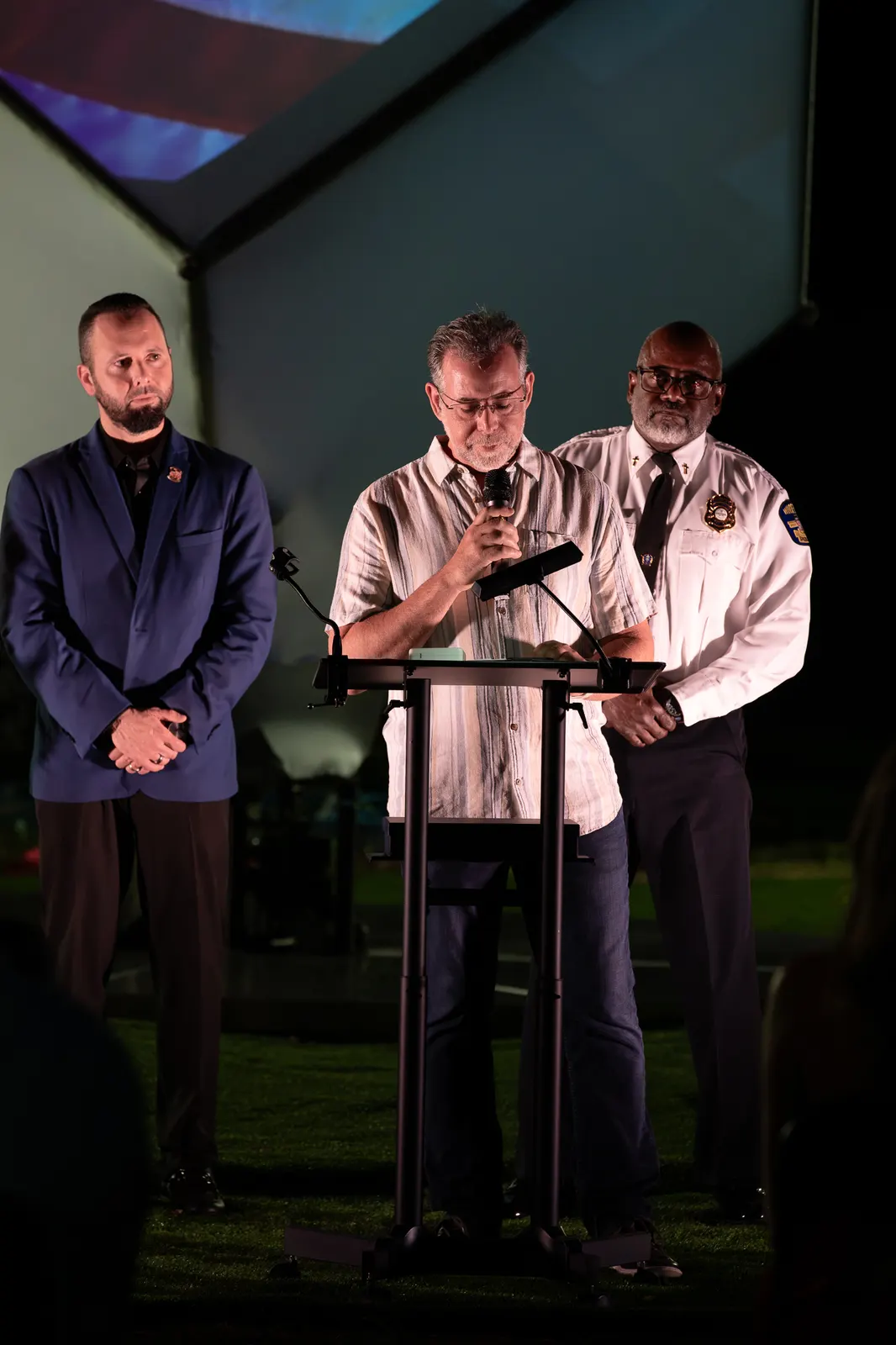 Two men stand together at the lectern with a uniformed official nearby.