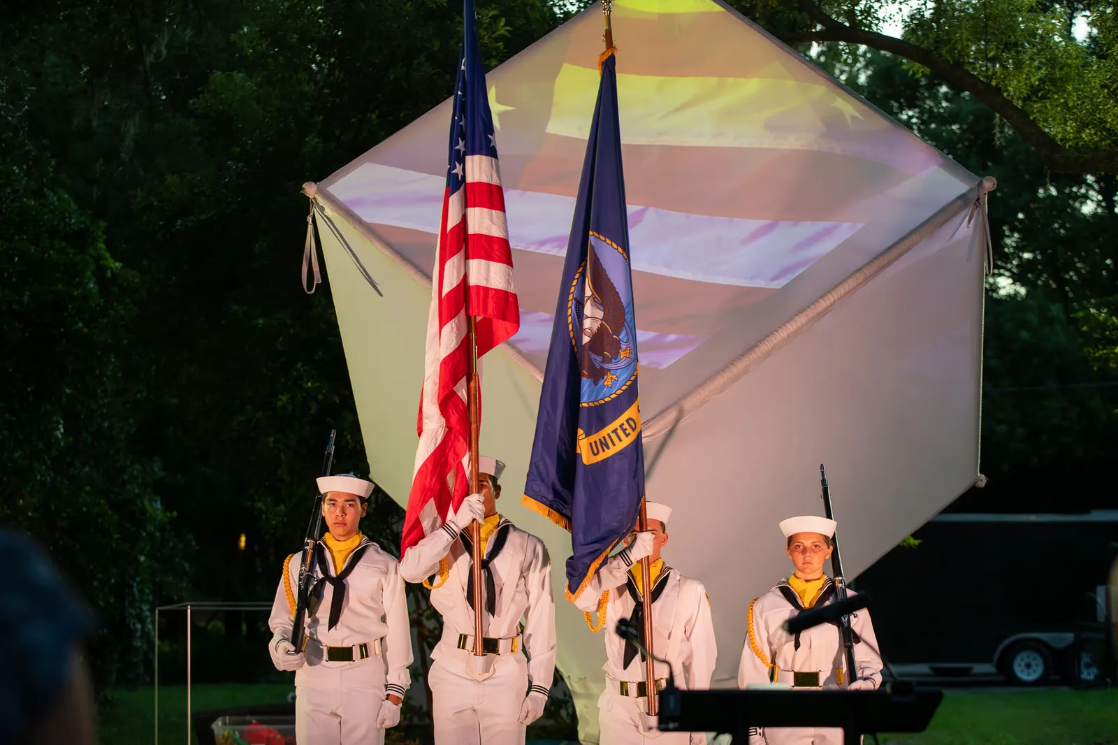The color guard pauses near a small table in front of the glowing cube.