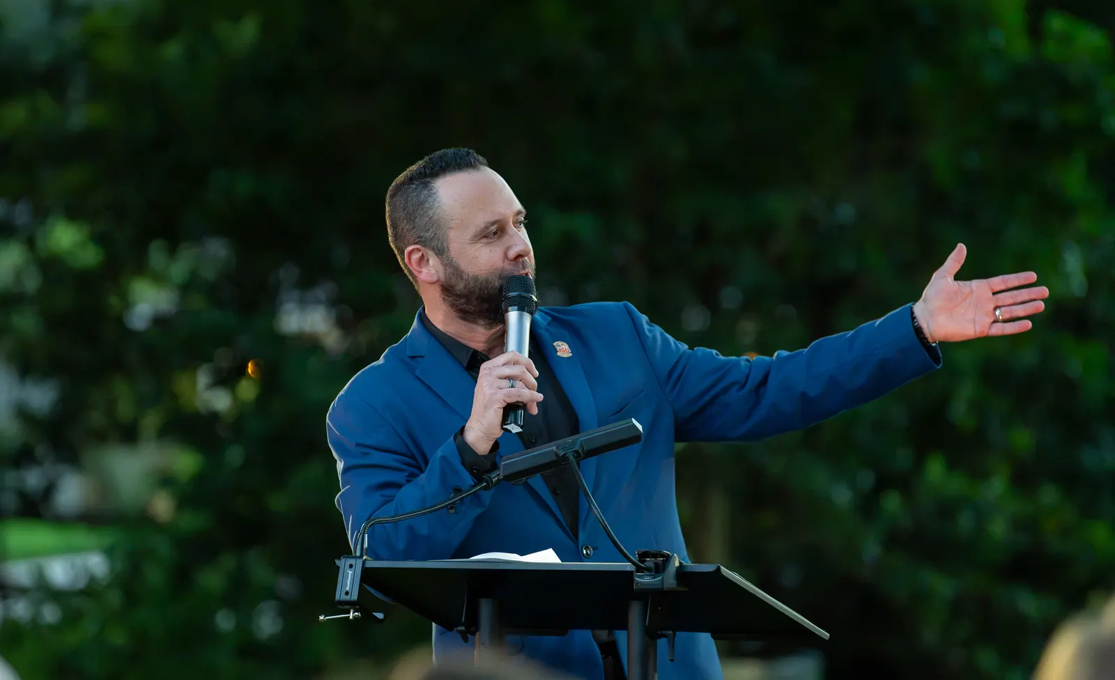 The speaker gestures toward the audience while holding a microphone.
