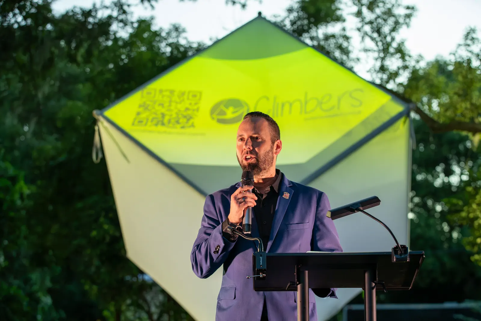 A man speaks beneath the Rise Up logo projected on the cube.