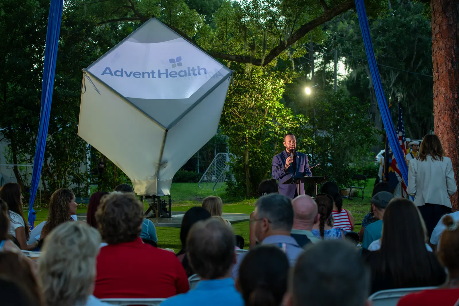 Two presenters stand before an AdventHealth logo projected on the cube.