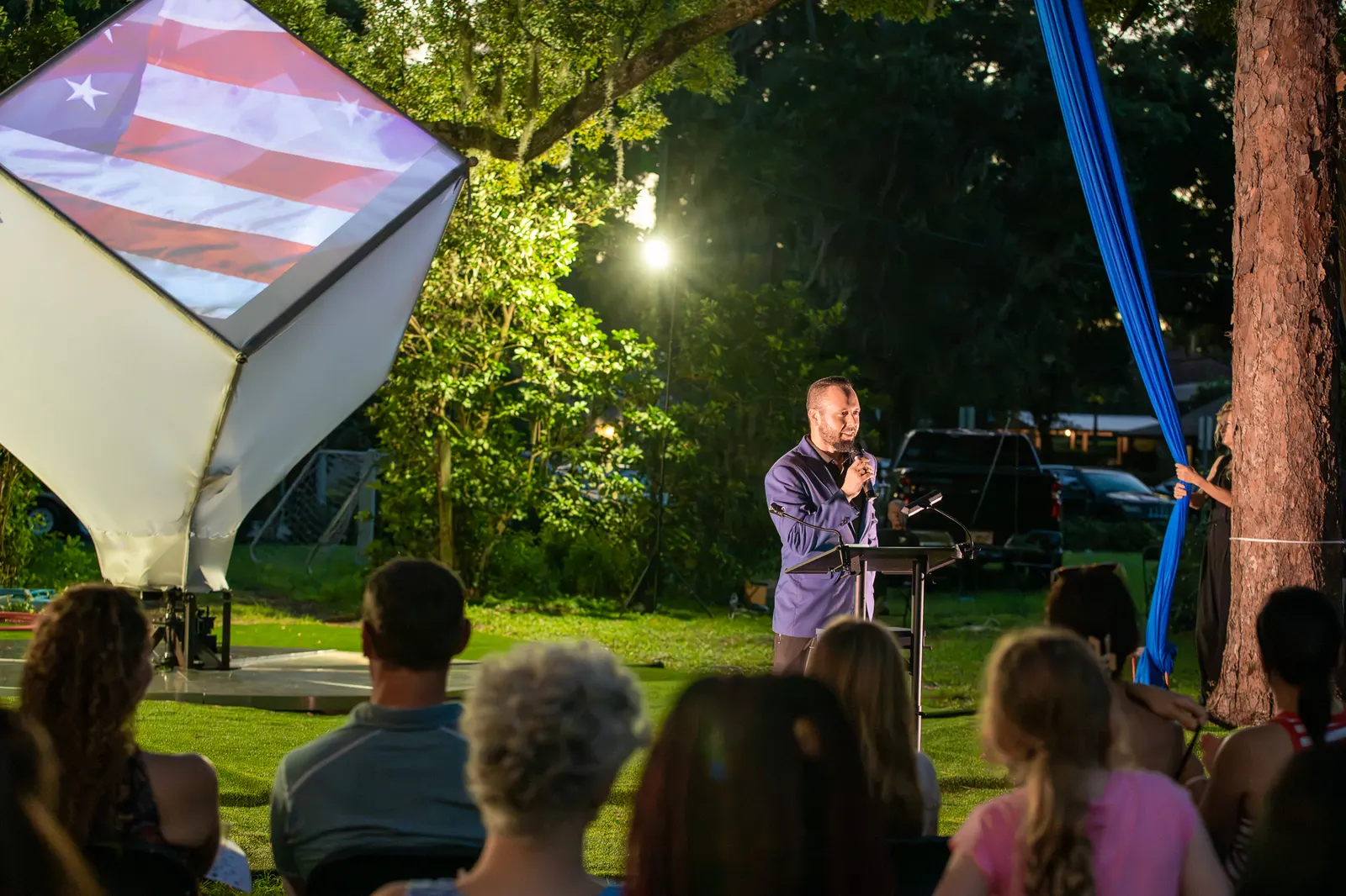 A speaker appears at the far side of the lawn beside the lit cube.