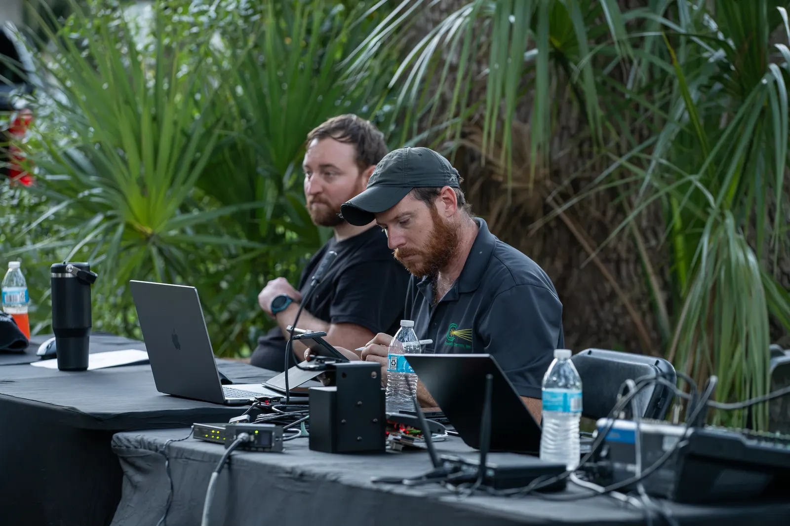 Two technicians manage sound equipment at an outdoor table.