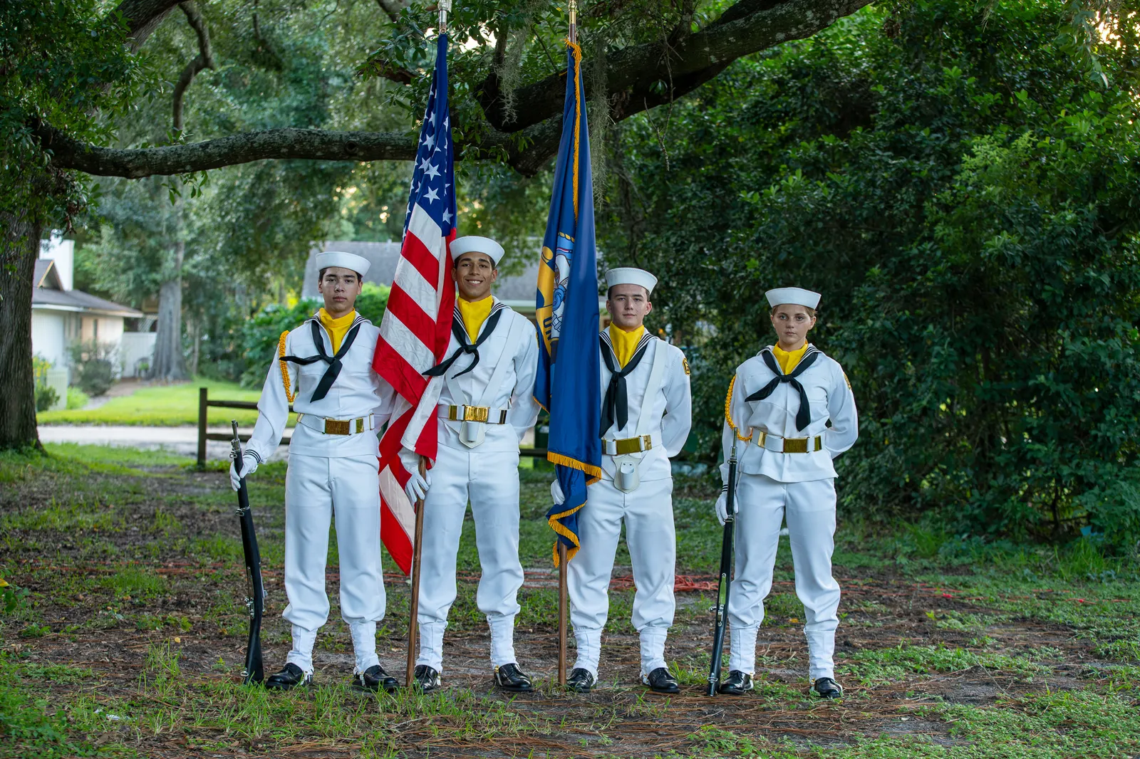 The Lone Sailor Division color guard stands beneath the trees with flags.