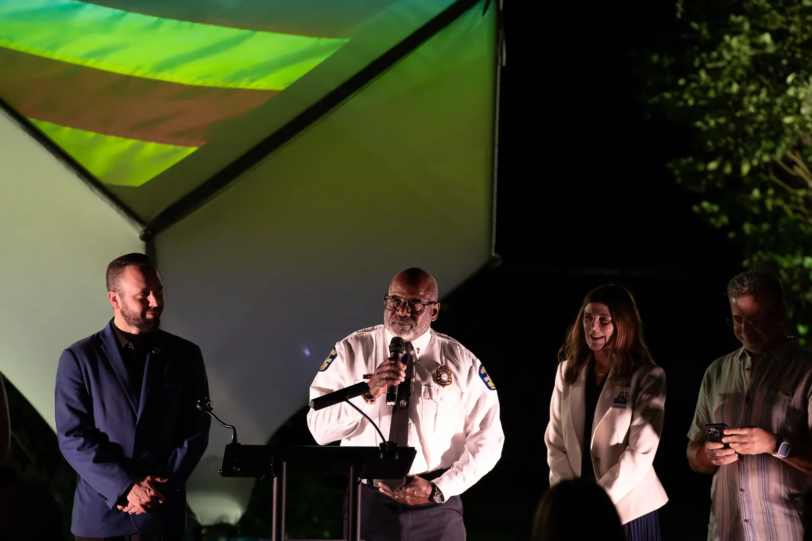 A uniformed official speaks at the lectern with community leaders beside him.