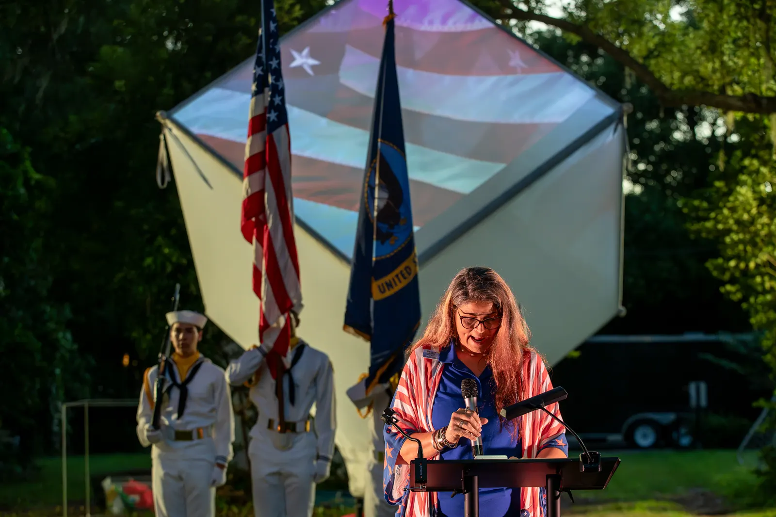 A woman reads from the lectern with the color guard behind her.