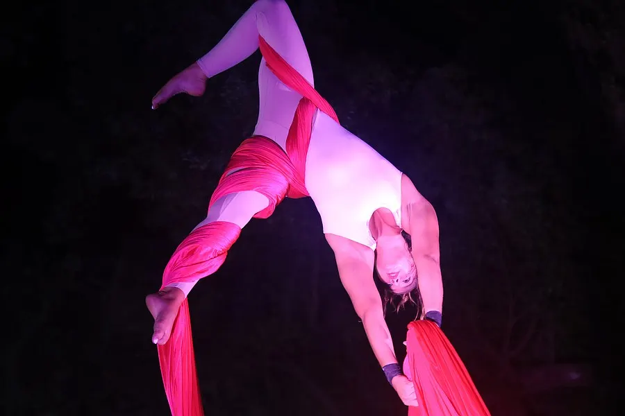 An aerialist arches backward while suspended beneath red light.