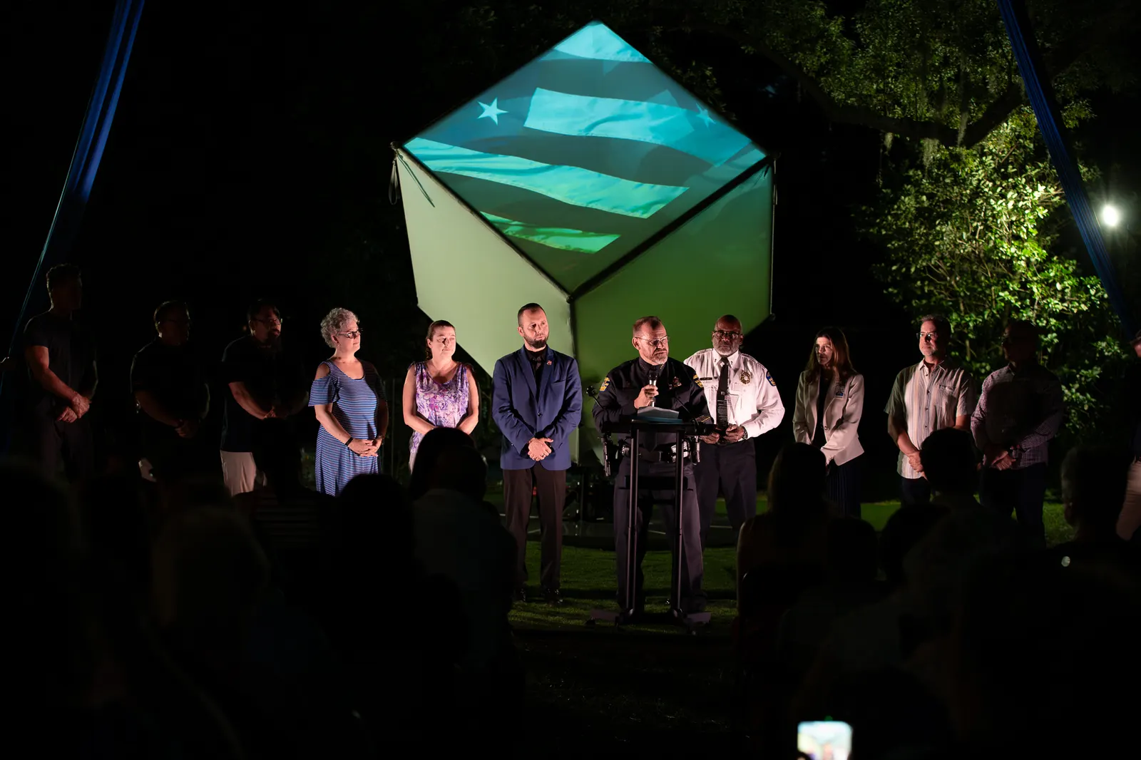 A woman speaks into a microphone with several honorees behind her.
