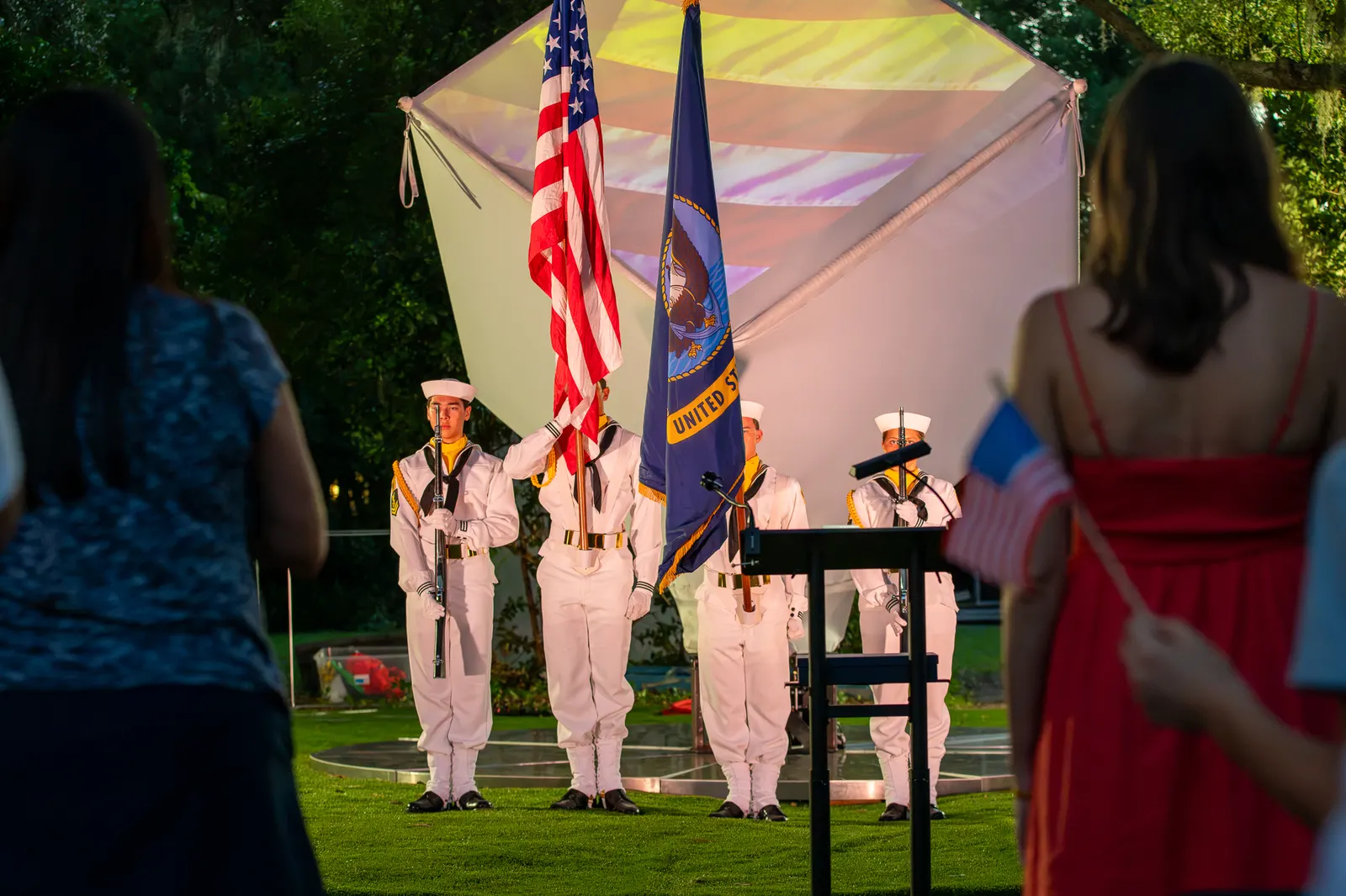 The color guard faces the stage while a woman in red stands in the foreground.
