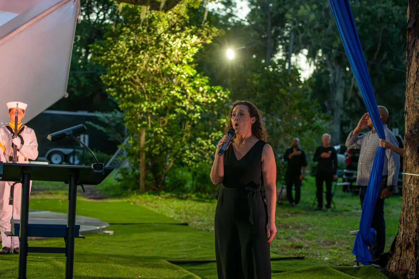 A singer performs on the lawn with the Sea Cadets behind her.