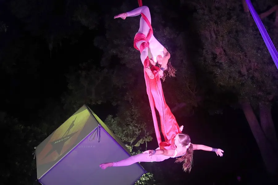 A performer hangs inverted above the illuminated geometric stage.