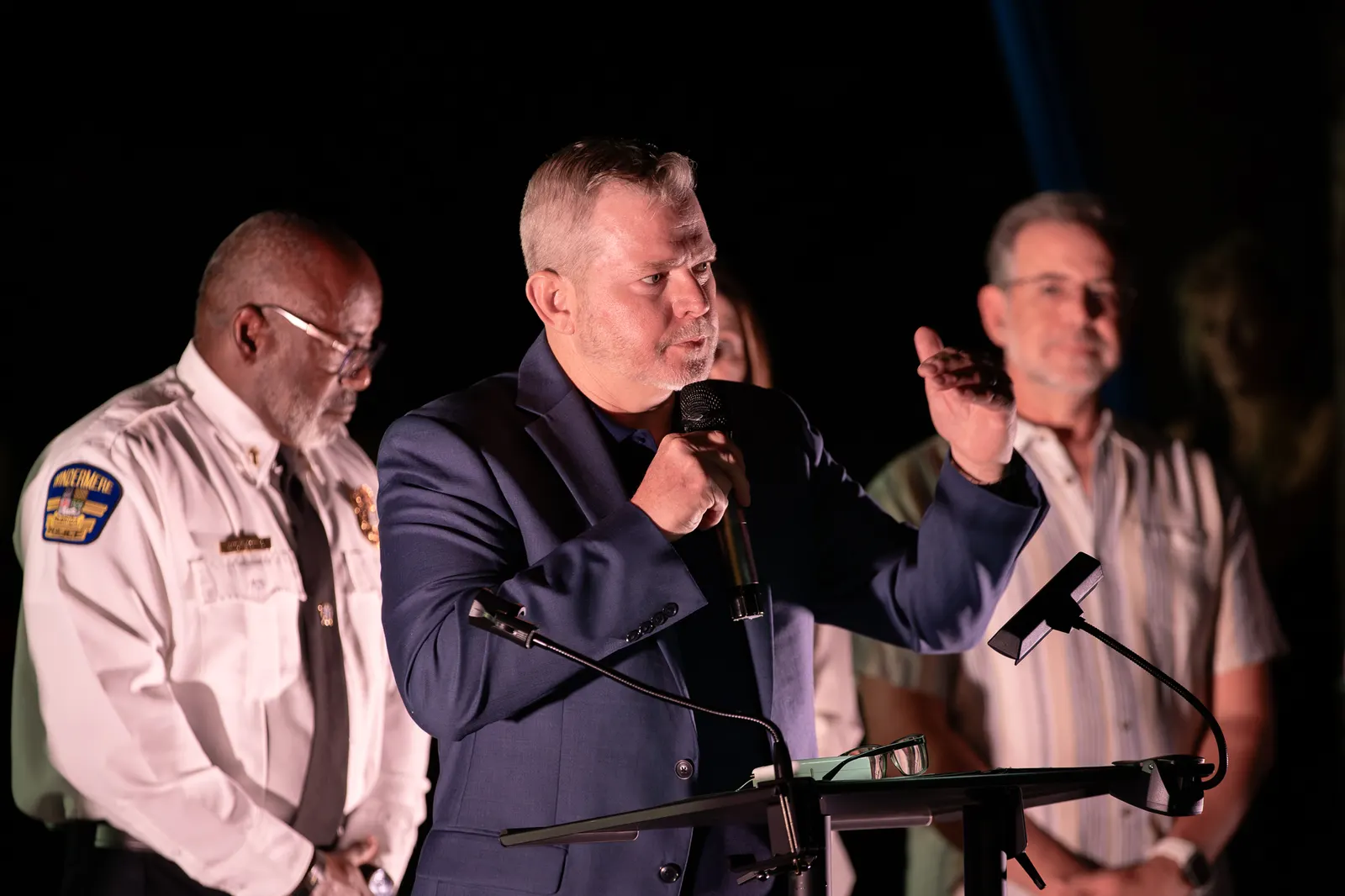 A man at the lectern gestures toward a uniformed official beside him.