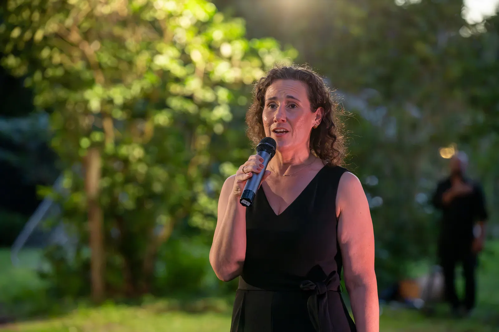 A woman sings into a handheld microphone outdoors.