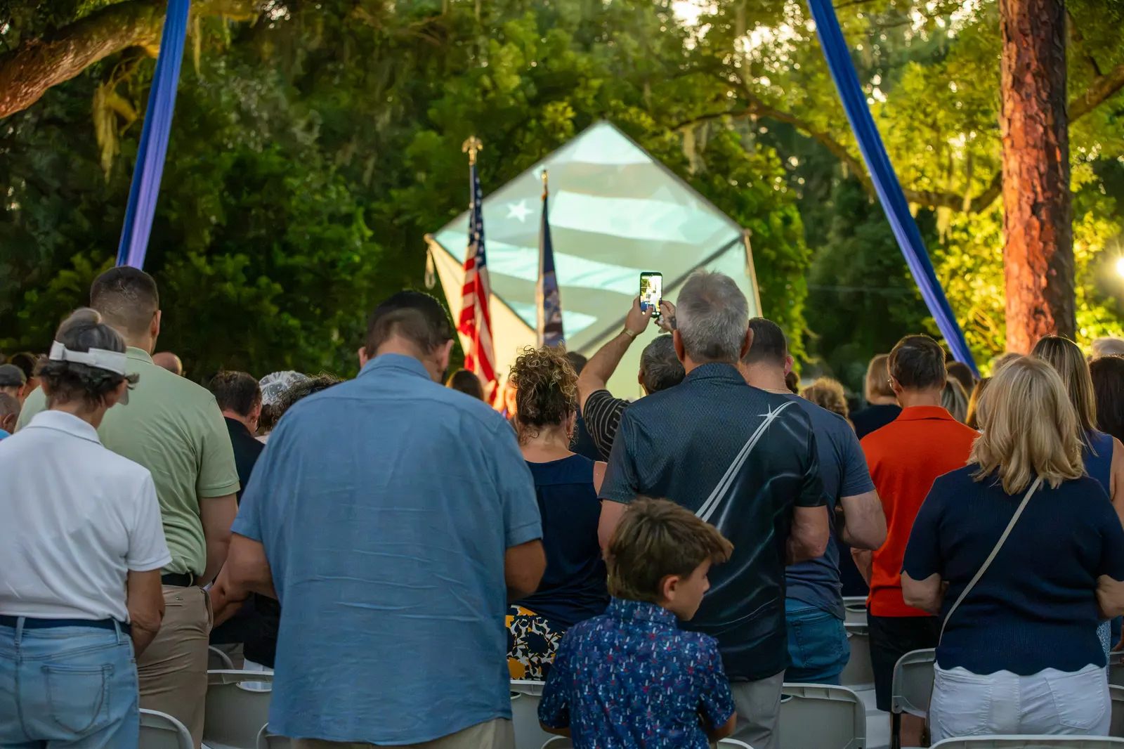 Audience members stand facing the stage during the ceremony.