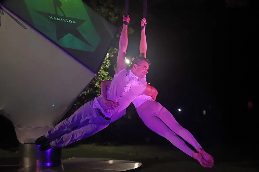 An aerialist stretches into a wide horizontal pose on blue silks.