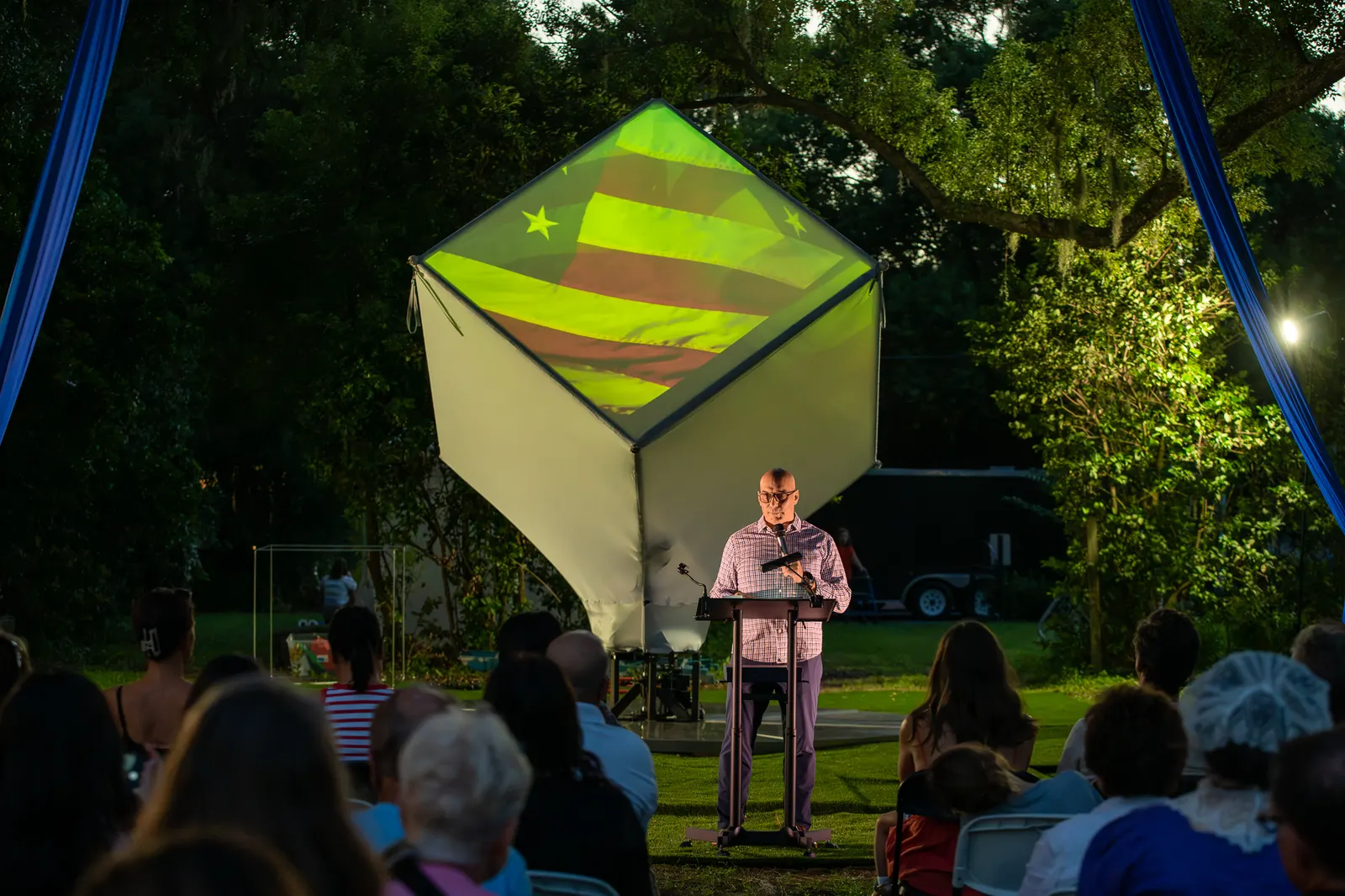 A man speaks alone at the lectern against green and purple light.
