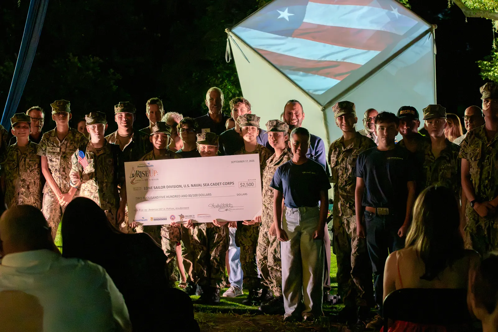 Cadets and community partners smile while holding the donation check.
