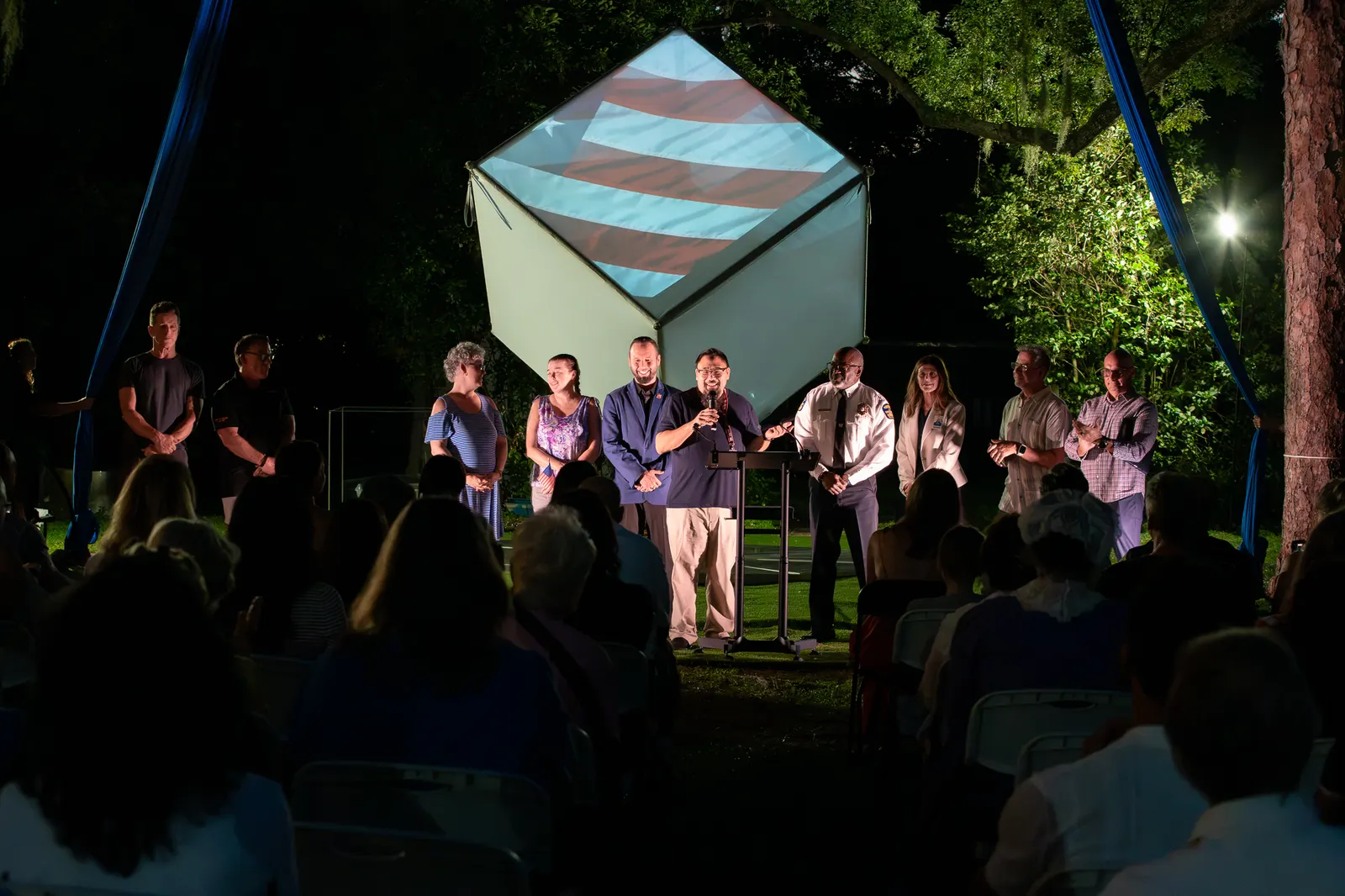 The purple-clad speaker addresses the seated audience from center stage.