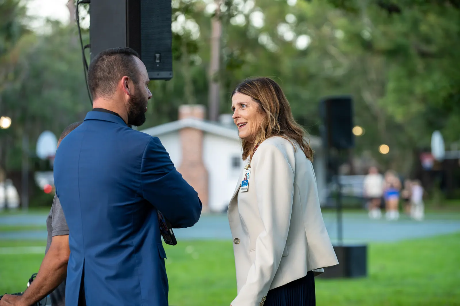 A man in a blue jacket greets a woman on the event lawn.