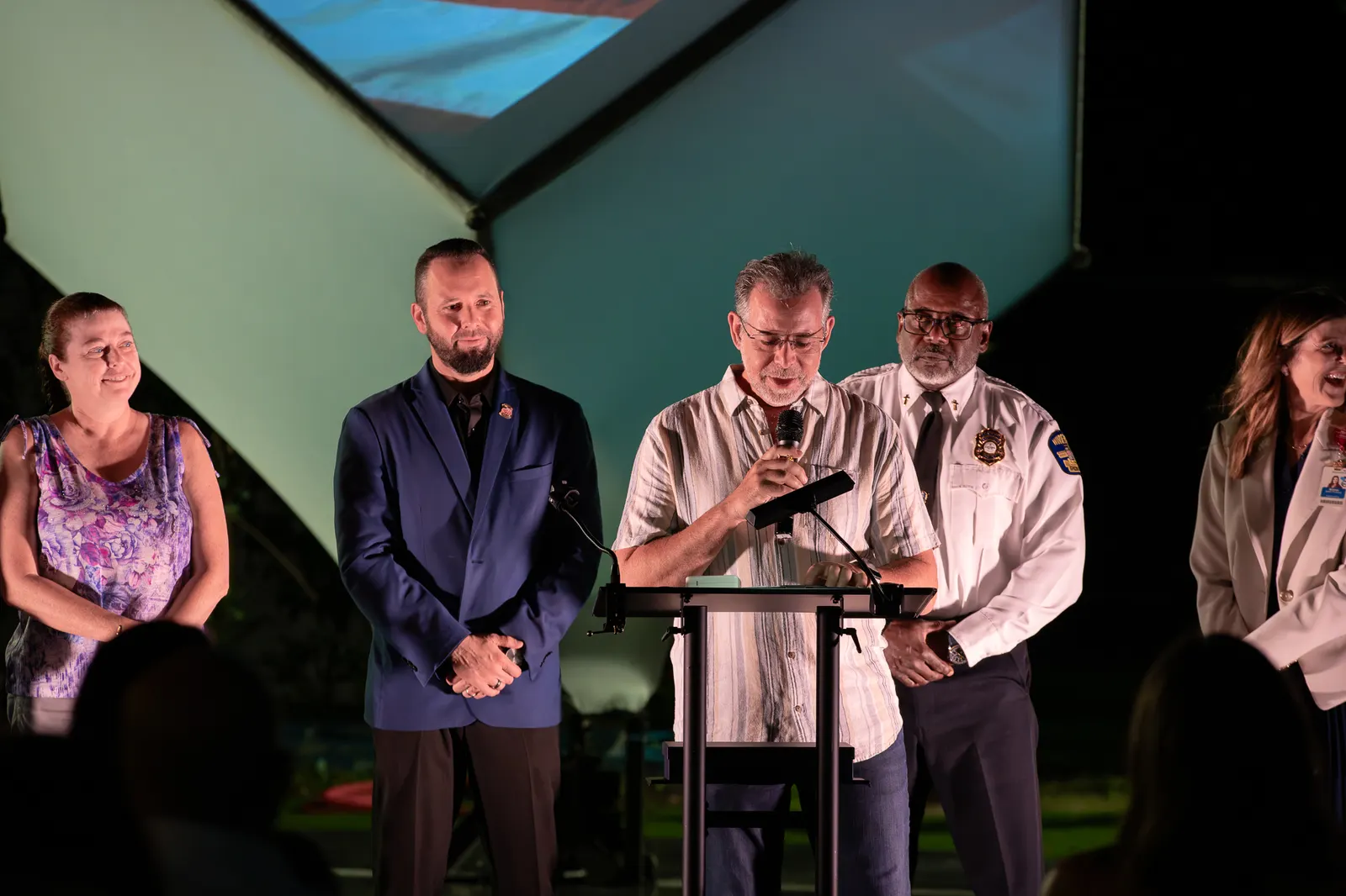 A vertical view shows the uniformed official speaking beside other honorees.