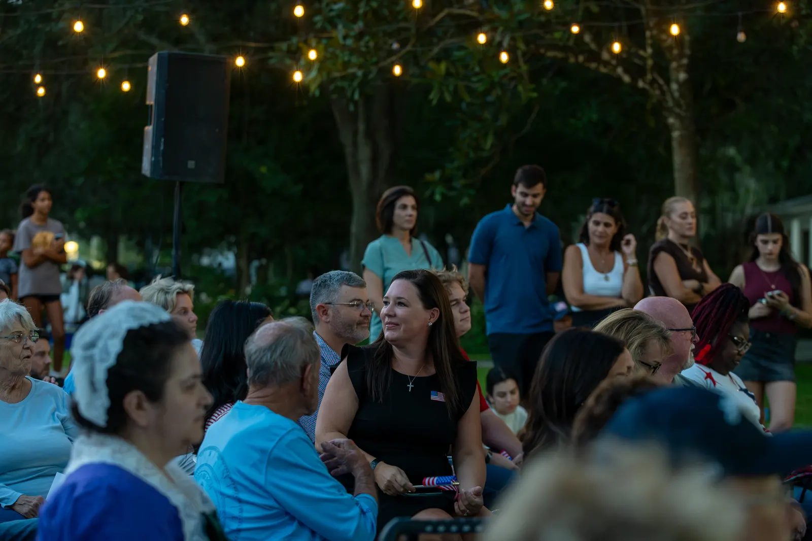 Guests seated beneath string lights watch the evening program.