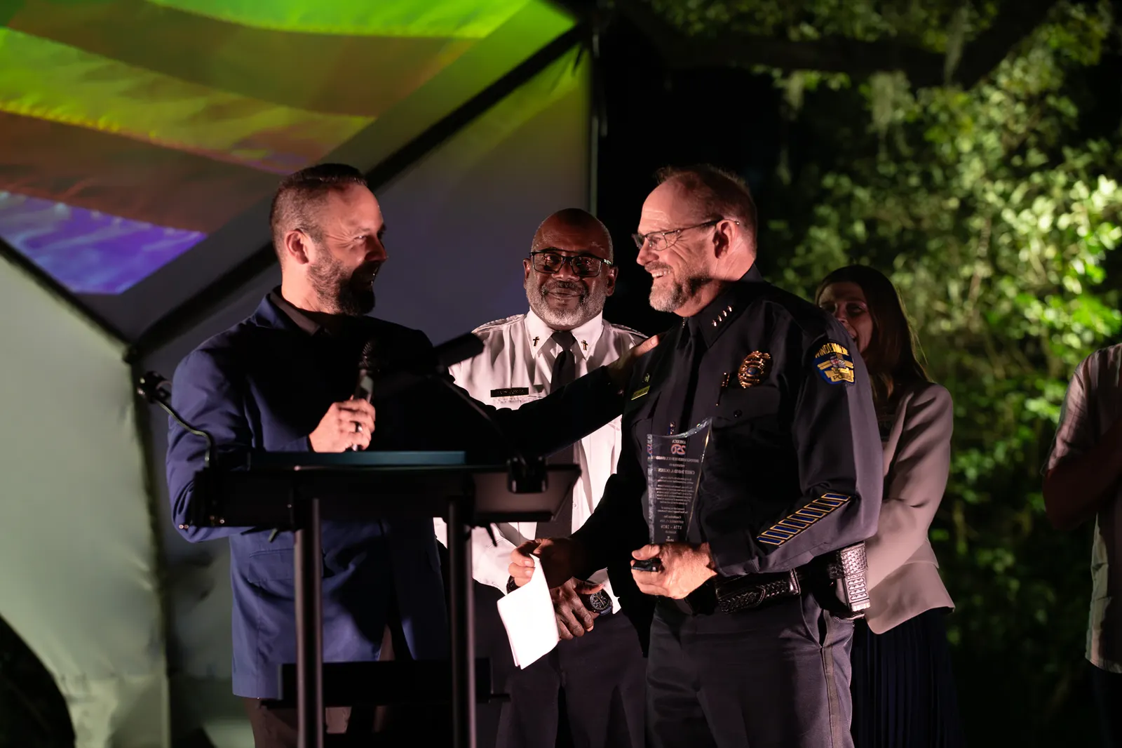 A presenter reaches toward a man at center stage during the recognition.