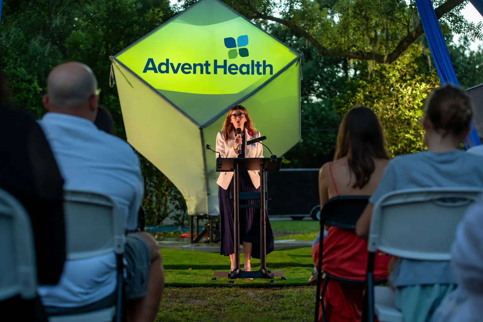 A woman addresses the audience from the lectern on the lawn.