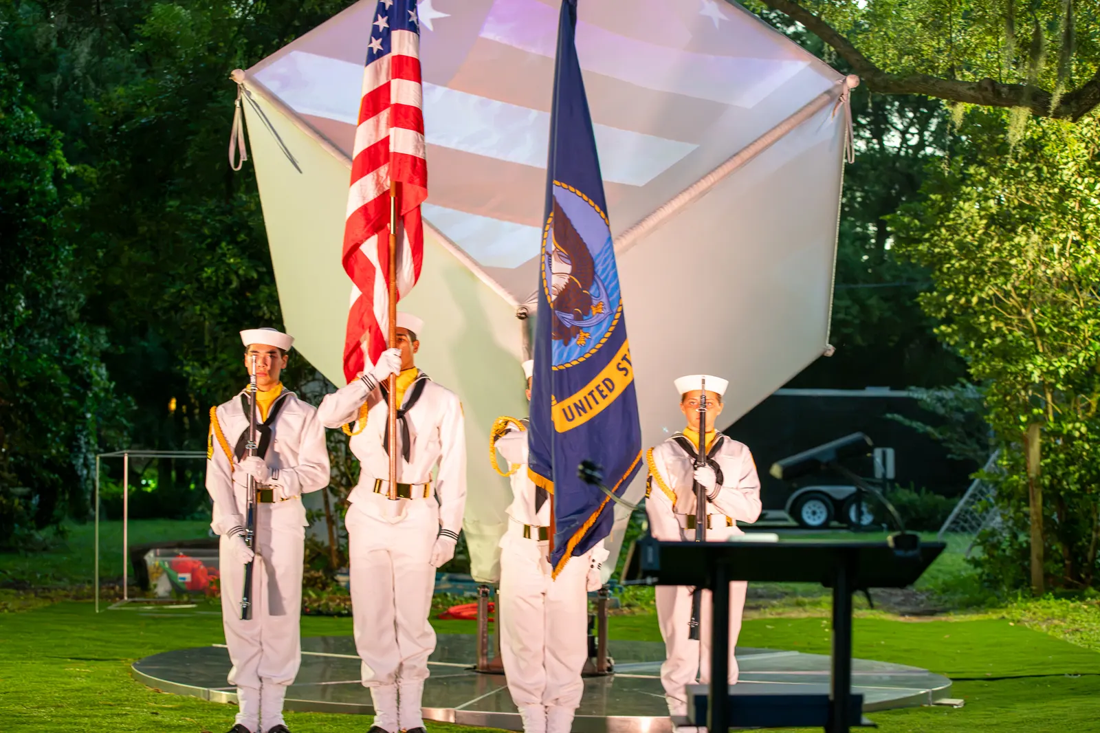 The color guard stands behind a singer near the illuminated cube.