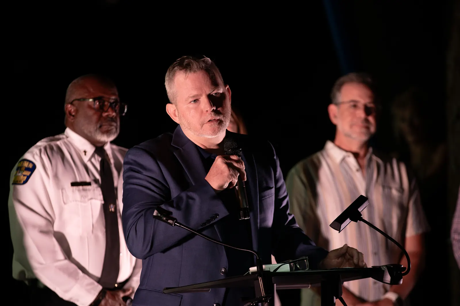 The uniformed official and two presenters share the microphone onstage.