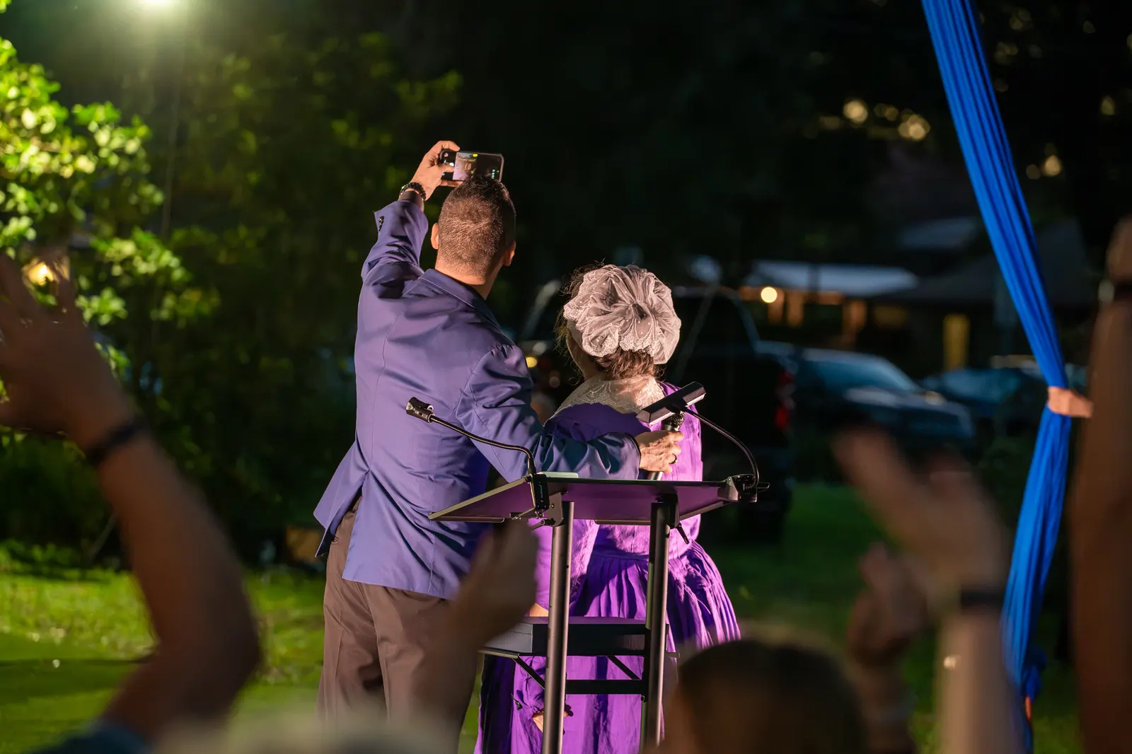A speaker points above the audience as his companion follows his gaze.