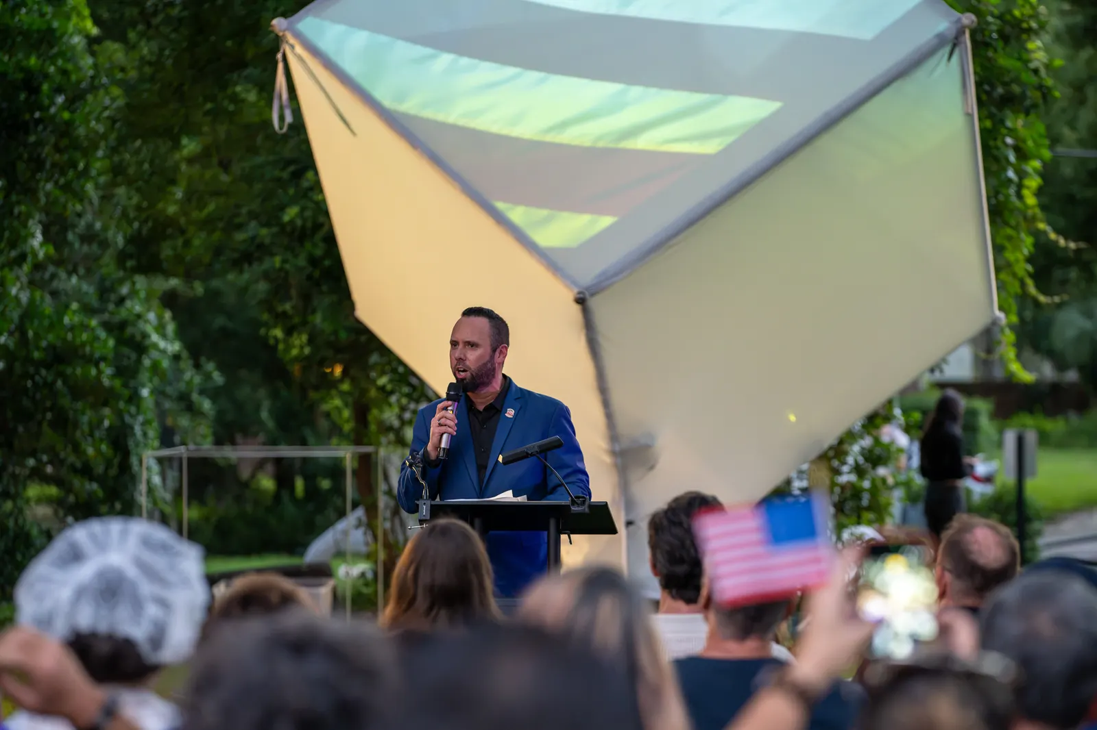 An evening speaker stands before the illuminated cube and seated guests.