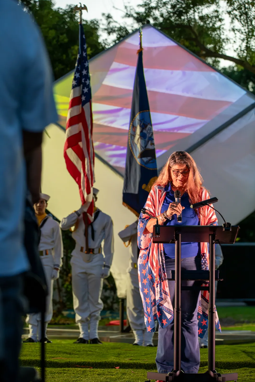A woman delivers remarks with uniformed Sea Cadets behind her.