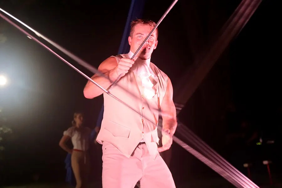 A performer balances across taut aerial straps under a bright spotlight.